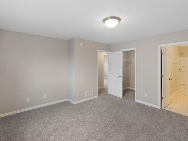 unfurnished bedroom featuring a walk in closet, connected bathroom, a closet, and light carpet