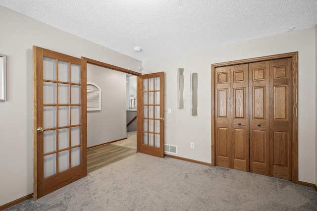 unfurnished bedroom with french doors, a closet, light carpet, and a textured ceiling