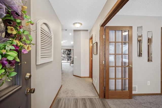 hallway with light colored carpet and a textured ceiling