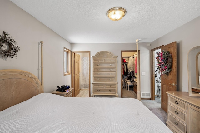 bedroom with connected bathroom, a spacious closet, light colored carpet, a textured ceiling, and a closet