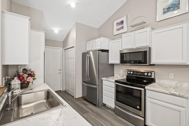 kitchen with lofted ceiling, sink, white cabinetry, light stone counters, and stainless steel appliances