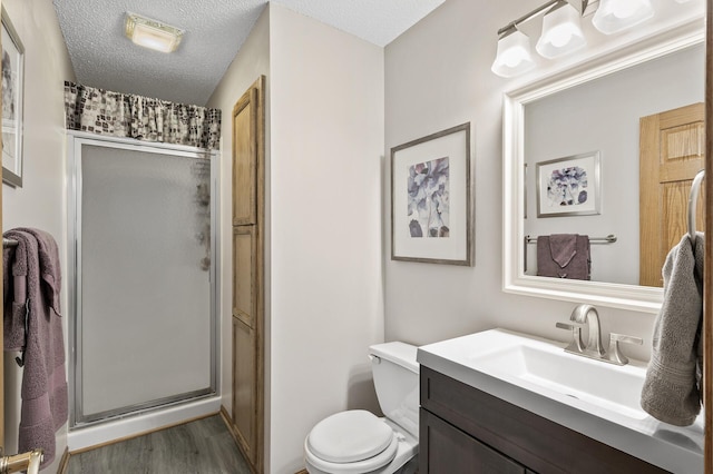 bathroom with a shower with shower door, hardwood / wood-style flooring, vanity, toilet, and a textured ceiling