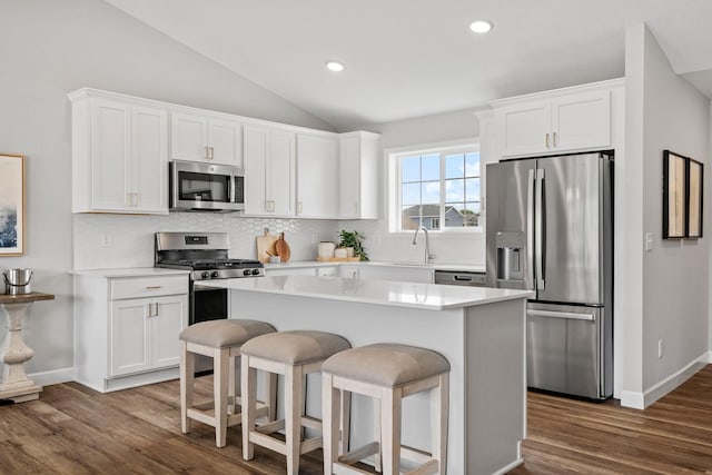 kitchen featuring a kitchen breakfast bar, stainless steel appliances, a center island, white cabinets, and vaulted ceiling