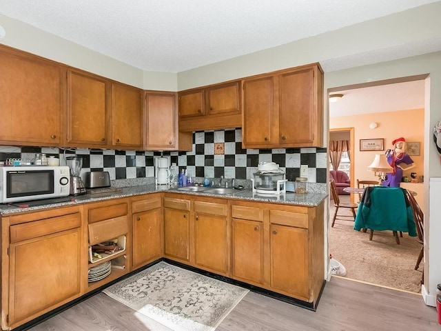 kitchen with sink, backsplash, light stone countertops, and light hardwood / wood-style floors