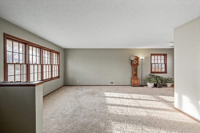 carpeted spare room with visible vents, a textured ceiling, and baseboards