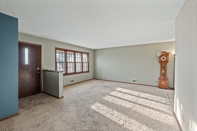 unfurnished living room with visible vents, baseboards, carpet, and a textured ceiling