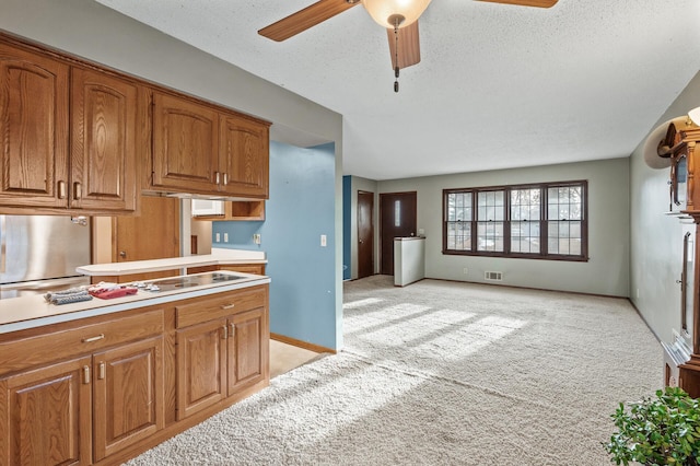 kitchen featuring brown cabinetry, visible vents, freestanding refrigerator, light countertops, and light colored carpet