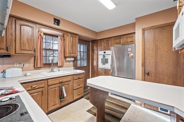 kitchen with brown cabinetry, light floors, white appliances, and a sink