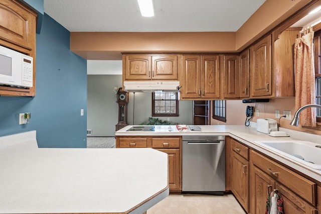 kitchen featuring a peninsula, a sink, light countertops, under cabinet range hood, and dishwasher