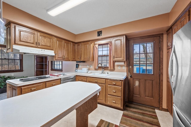 kitchen featuring under cabinet range hood, light countertops, brown cabinets, appliances with stainless steel finishes, and a sink