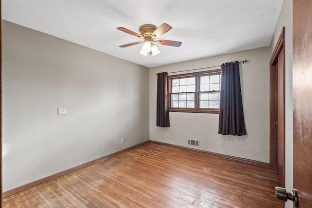 spare room with a ceiling fan, visible vents, light wood finished floors, and baseboards