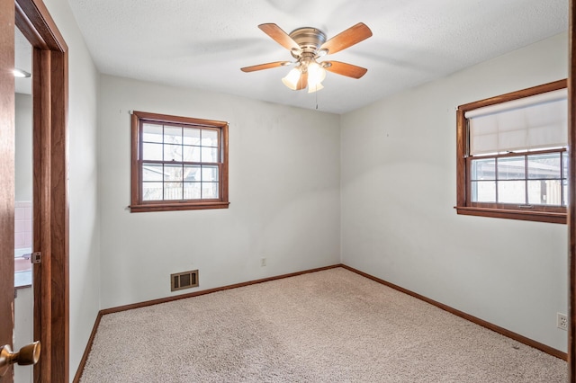 carpeted spare room featuring a textured ceiling, baseboards, visible vents, and ceiling fan