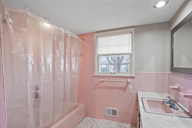 bathroom featuring vanity, visible vents, shower / tub combo, a textured ceiling, and tile walls