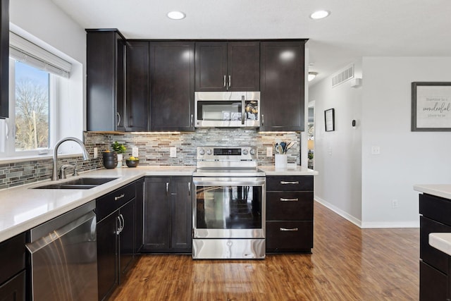 kitchen featuring appliances with stainless steel finishes, wood-type flooring, sink, dark brown cabinetry, and tasteful backsplash