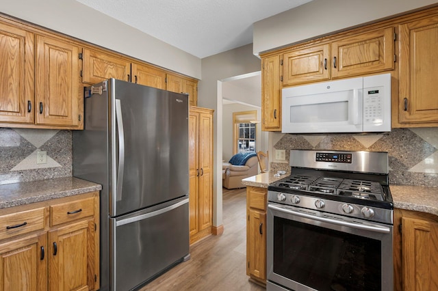 kitchen featuring tasteful backsplash, appliances with stainless steel finishes, light hardwood / wood-style flooring, and a textured ceiling