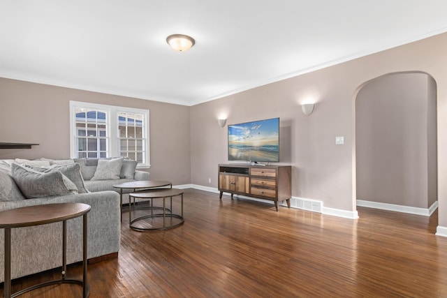 living room with arched walkways, visible vents, ornamental molding, baseboards, and hardwood / wood-style flooring