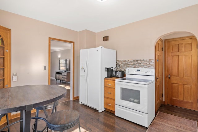 kitchen featuring arched walkways, white appliances, dark wood-type flooring, baseboards, and tasteful backsplash