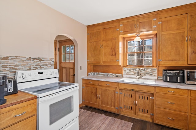 kitchen with white electric range oven, light countertops, a sink, and brown cabinetry