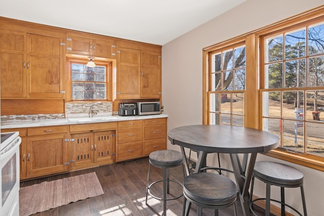 kitchen with electric range, a sink, brown cabinets, decorative backsplash, and stainless steel microwave