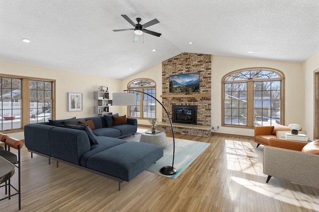 living room with a fireplace, light wood-type flooring, lofted ceiling, ceiling fan, and a textured ceiling