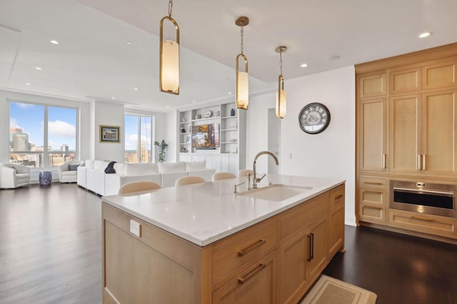 kitchen with sink, decorative light fixtures, oven, and a center island with sink