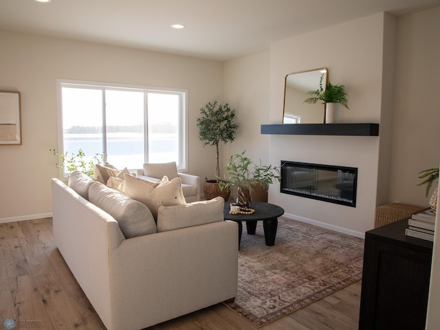 living area with light wood-style flooring, recessed lighting, a water view, baseboards, and a glass covered fireplace