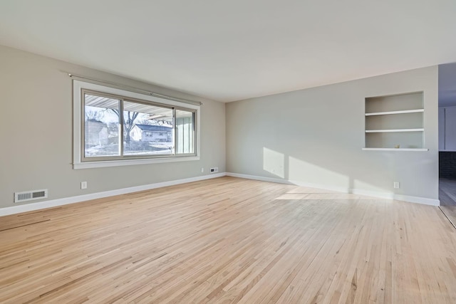 unfurnished living room featuring built in shelves and light wood-type flooring