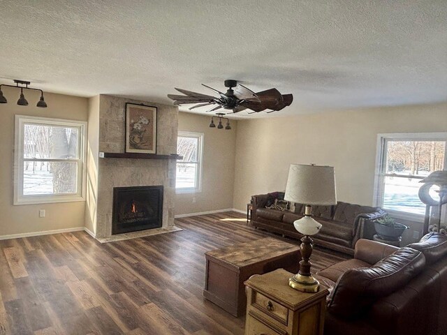 living area featuring baseboards, dark wood finished floors, ceiling fan, a textured ceiling, and a fireplace