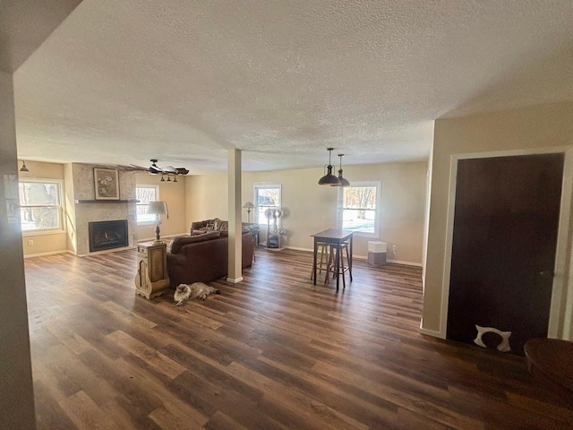 living room featuring baseboards, ceiling fan, dark wood-type flooring, a textured ceiling, and a fireplace