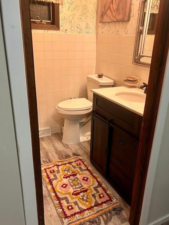 half bath featuring toilet, a wainscoted wall, tile walls, vanity, and wallpapered walls