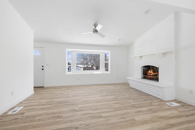 unfurnished living room with ceiling fan, vaulted ceiling, a brick fireplace, and light wood-type flooring