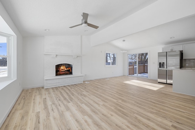 unfurnished living room with vaulted ceiling, a fireplace, ceiling fan, light hardwood / wood-style floors, and a textured ceiling