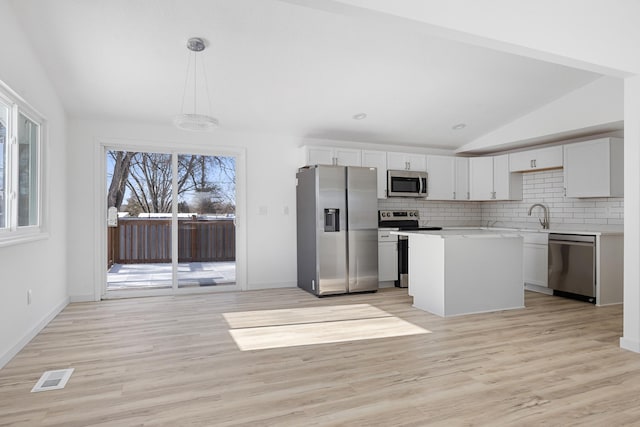 kitchen featuring tasteful backsplash, vaulted ceiling, hanging light fixtures, appliances with stainless steel finishes, and white cabinets