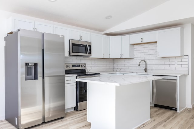 kitchen featuring a kitchen island, white cabinetry, lofted ceiling, stainless steel appliances, and light stone countertops