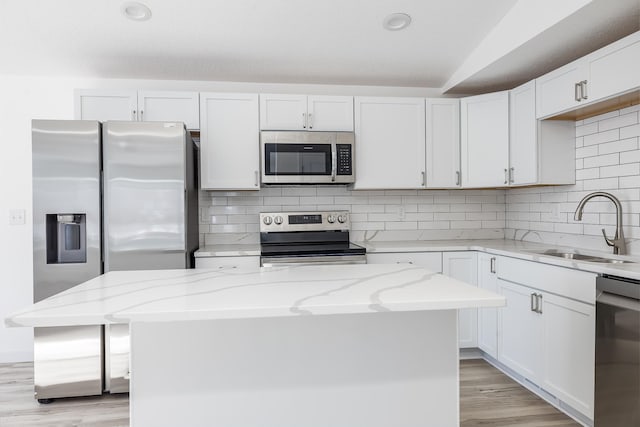 kitchen with appliances with stainless steel finishes, a center island, sink, and light stone countertops