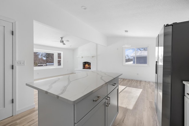 kitchen with vaulted ceiling, gray cabinetry, hanging light fixtures, a center island, and light stone counters