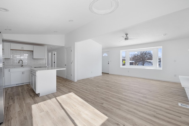 kitchen with vaulted ceiling, a kitchen island, backsplash, and light hardwood / wood-style flooring