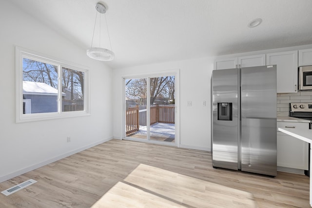 kitchen with tasteful backsplash, light hardwood / wood-style flooring, hanging light fixtures, stainless steel appliances, and white cabinets