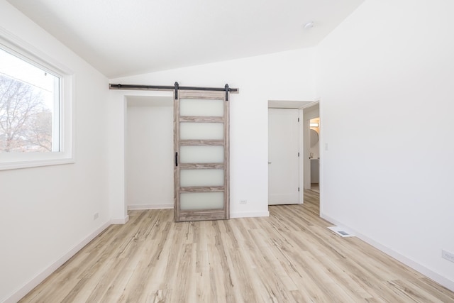 unfurnished bedroom featuring vaulted ceiling, a barn door, and light wood-type flooring