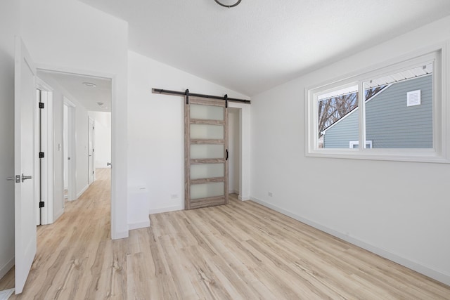 unfurnished bedroom featuring vaulted ceiling, light hardwood / wood-style floors, and a barn door