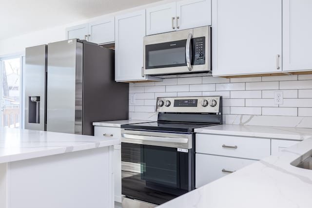 kitchen featuring appliances with stainless steel finishes, white cabinets, light stone counters, and decorative backsplash