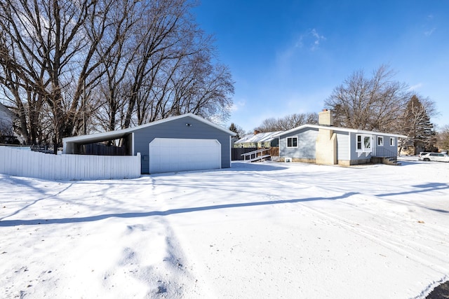 view of snow covered exterior featuring a garage, a carport, and an outbuilding