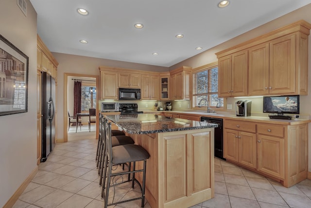 kitchen featuring a breakfast bar, sink, dark stone countertops, a kitchen island, and black appliances