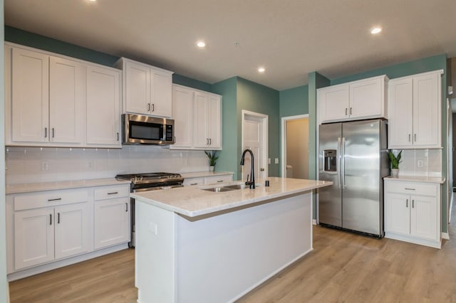 kitchen with light wood-type flooring, appliances with stainless steel finishes, white cabinets, and a sink