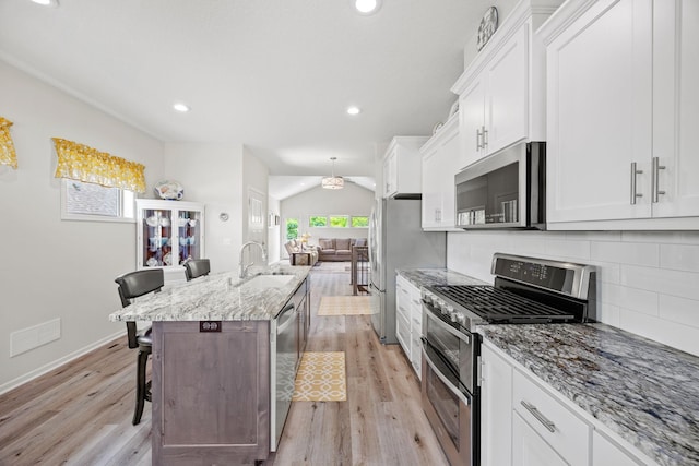 kitchen with sink, a breakfast bar, white cabinetry, stainless steel appliances, and light stone counters