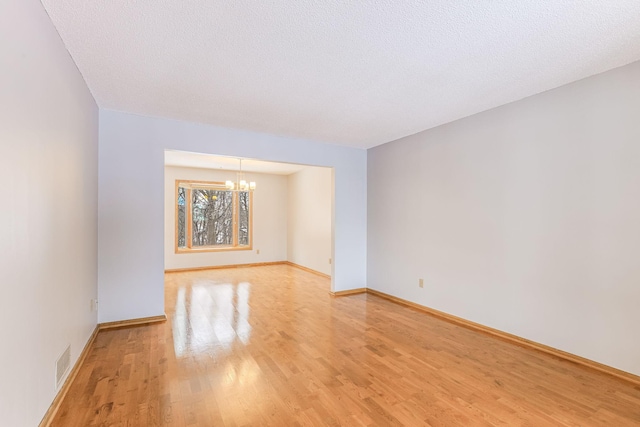 empty room with an inviting chandelier, light hardwood / wood-style floors, and a textured ceiling