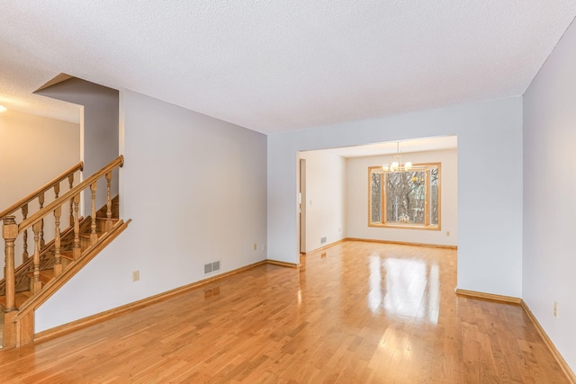 unfurnished room with an inviting chandelier, light hardwood / wood-style flooring, and a textured ceiling