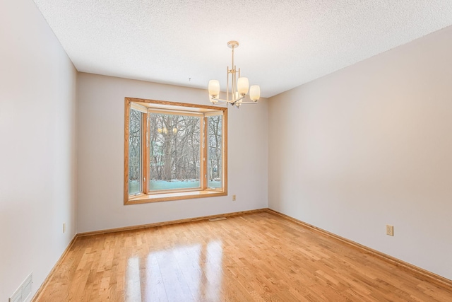 unfurnished room with an inviting chandelier, a textured ceiling, and light wood-type flooring