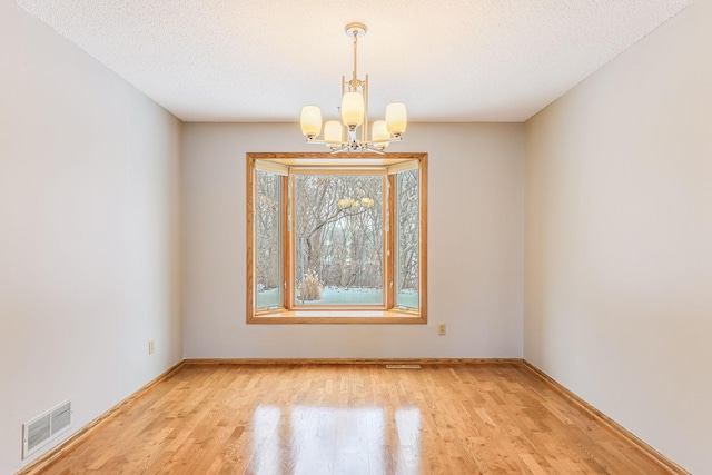 unfurnished room with a chandelier, a textured ceiling, and light hardwood / wood-style floors