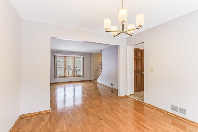 empty room featuring an inviting chandelier, light hardwood / wood-style flooring, and a textured ceiling